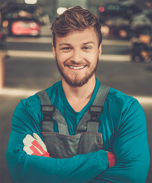 Junger Mann posiert lächelnd. Autowerkstatt im Hintergrund