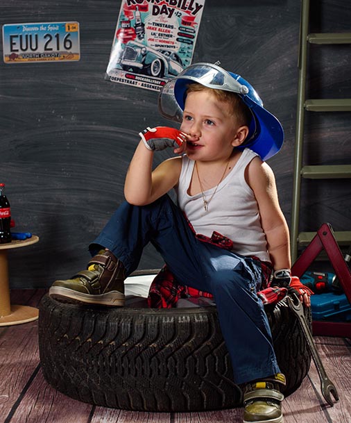 Kind in Handewerker-Köstum und Maulschlüssel auf einem LKW-Reifen. 